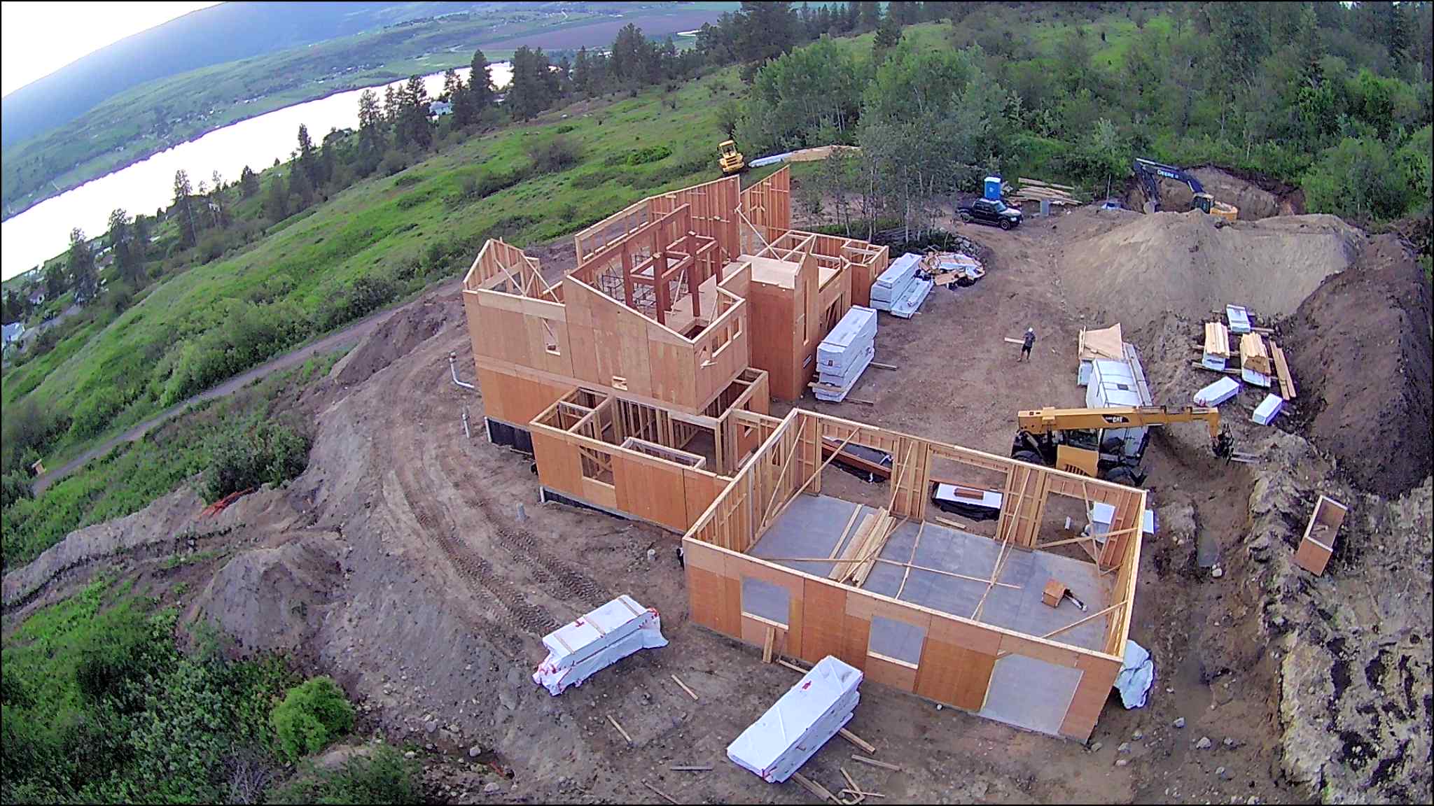 Aerial drone view of a panelized home under construction, showing the structural shell being assembled on a concrete foundation in a wooded area.