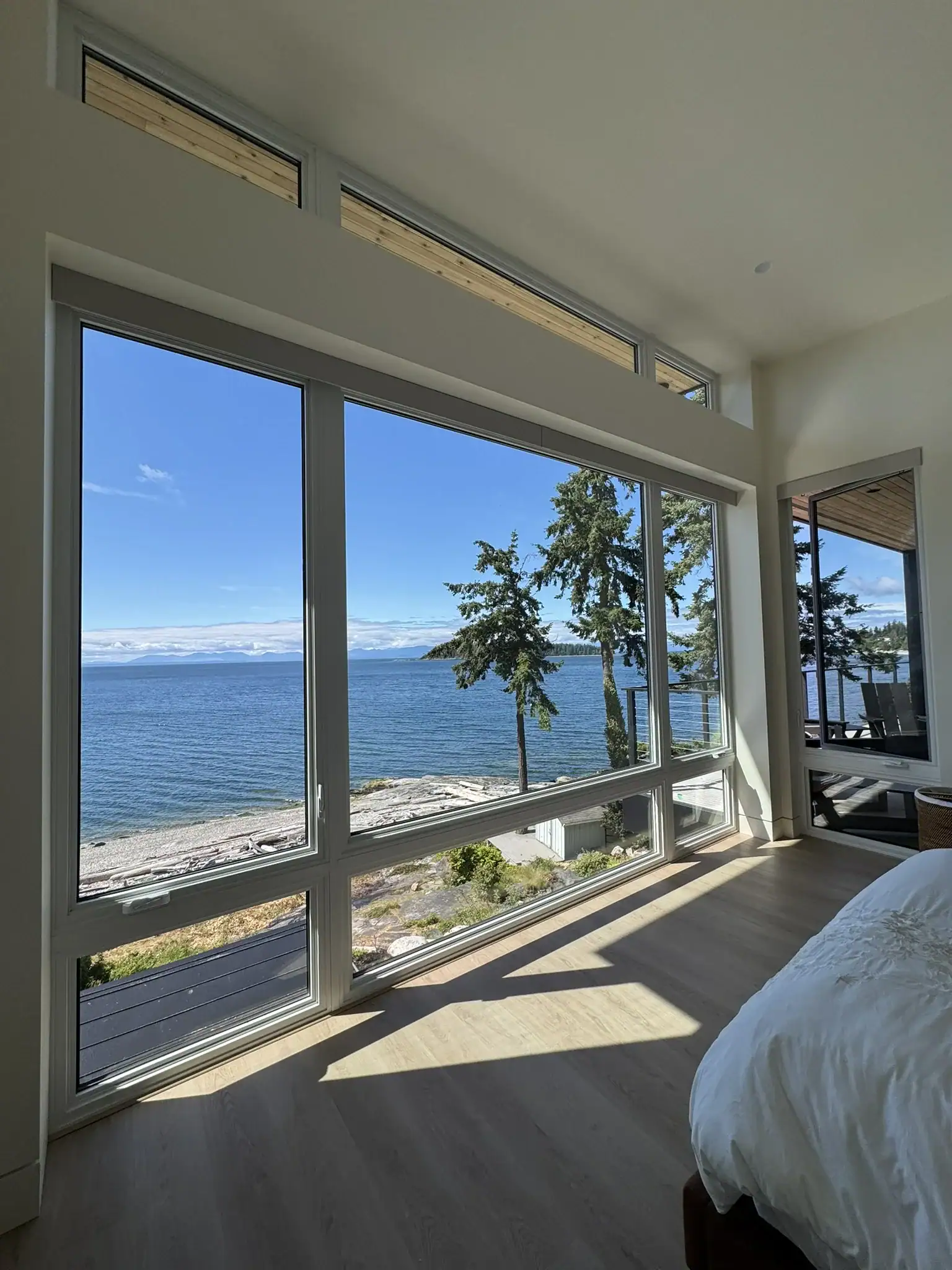 sunshine-coast-waterfront-home-bedroom-ocean-view Bedroom in a Sunshine Coast waterfront custom home with large windows framing the ocean view.